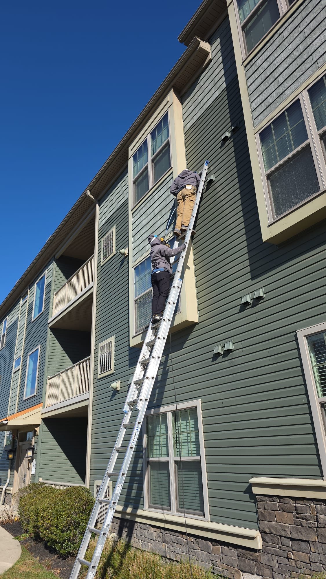 Technicians on a tall ladder servicing a condominium building