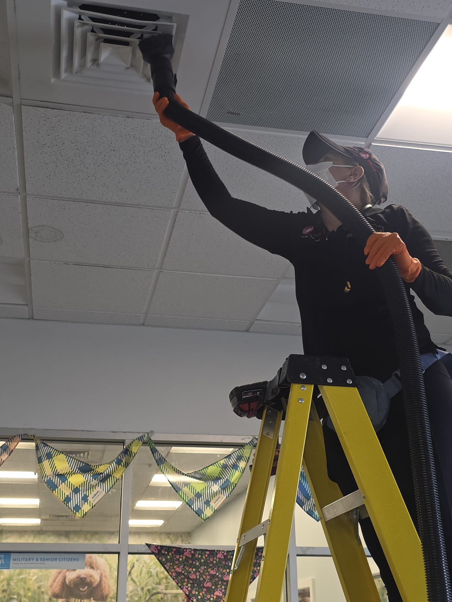 Technician vacuuming a ceiling vent inside a PetSmart