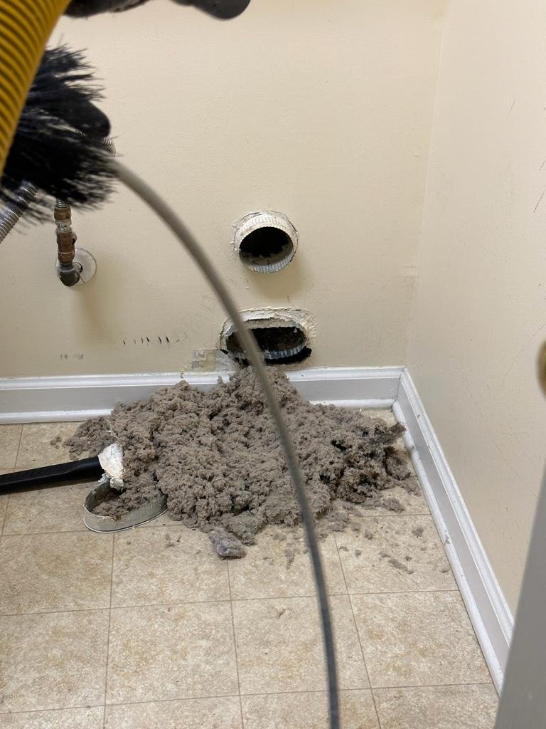 Pile of lint pulled from a dryer vent on the floor with cleaning tools