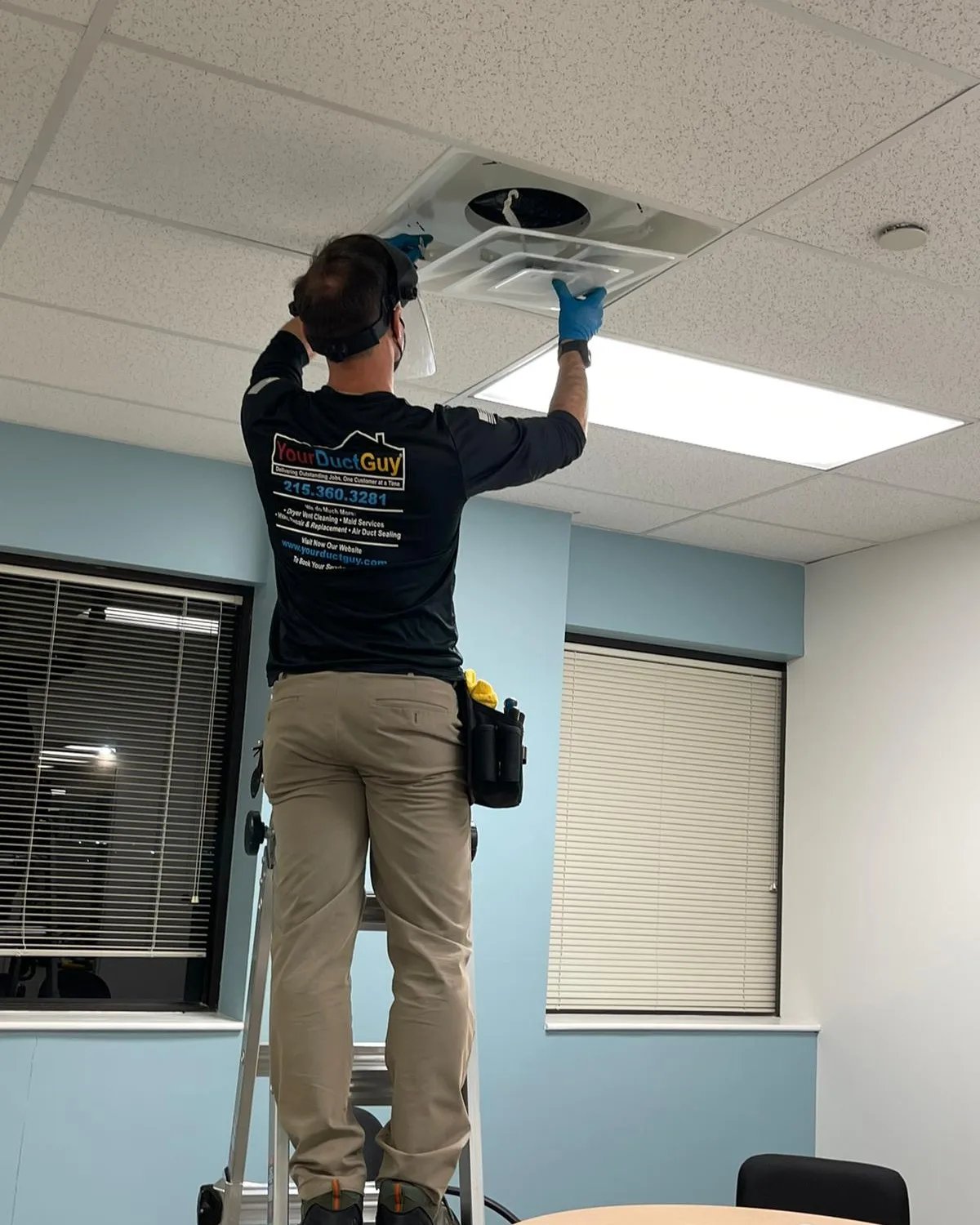 Your Duct Guy technician on a ladder cleaning a ceiling vent